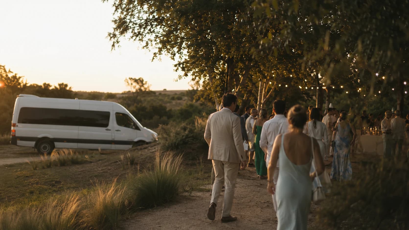 Invitados llegando a un casamiento al atardecer, con el minibús que los trasladó estacionado junto al camino